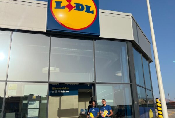 Dos personas sonrientes sosteniendo folletos frente a la tienda Lidl en El Médano, destacando la colaboración entre BlueFox y Lidl para acercar las marcas a los consumidores en el punto de venta.