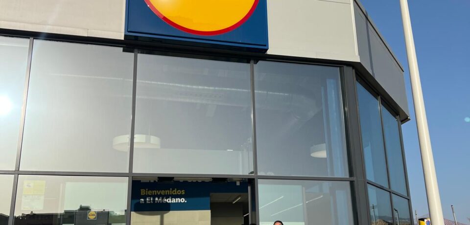 BlueFox Iberia - Lidl (3) Dos personas sonrientes sosteniendo folletos frente a la tienda Lidl en El Médano, destacando la colaboración entre BlueFox y Lidl para acercar las marcas a los consumidores en el punto de venta.