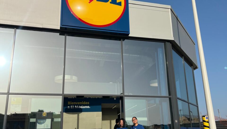 Dos personas sonrientes sosteniendo folletos frente a la tienda Lidl en El Médano, destacando la colaboración entre BlueFox y Lidl para acercar las marcas a los consumidores en el punto de venta.